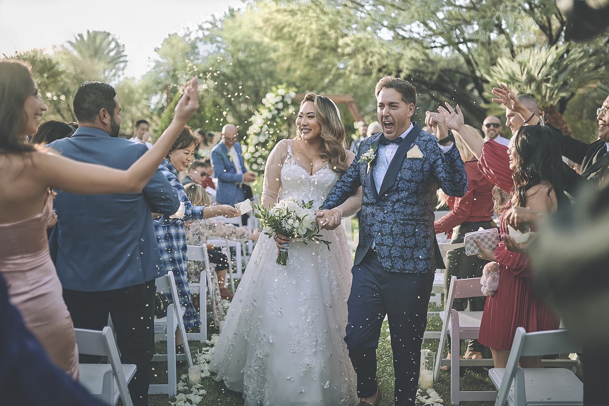 Newlyweds celebrate as guests toss flower petals during an outdoor recessional