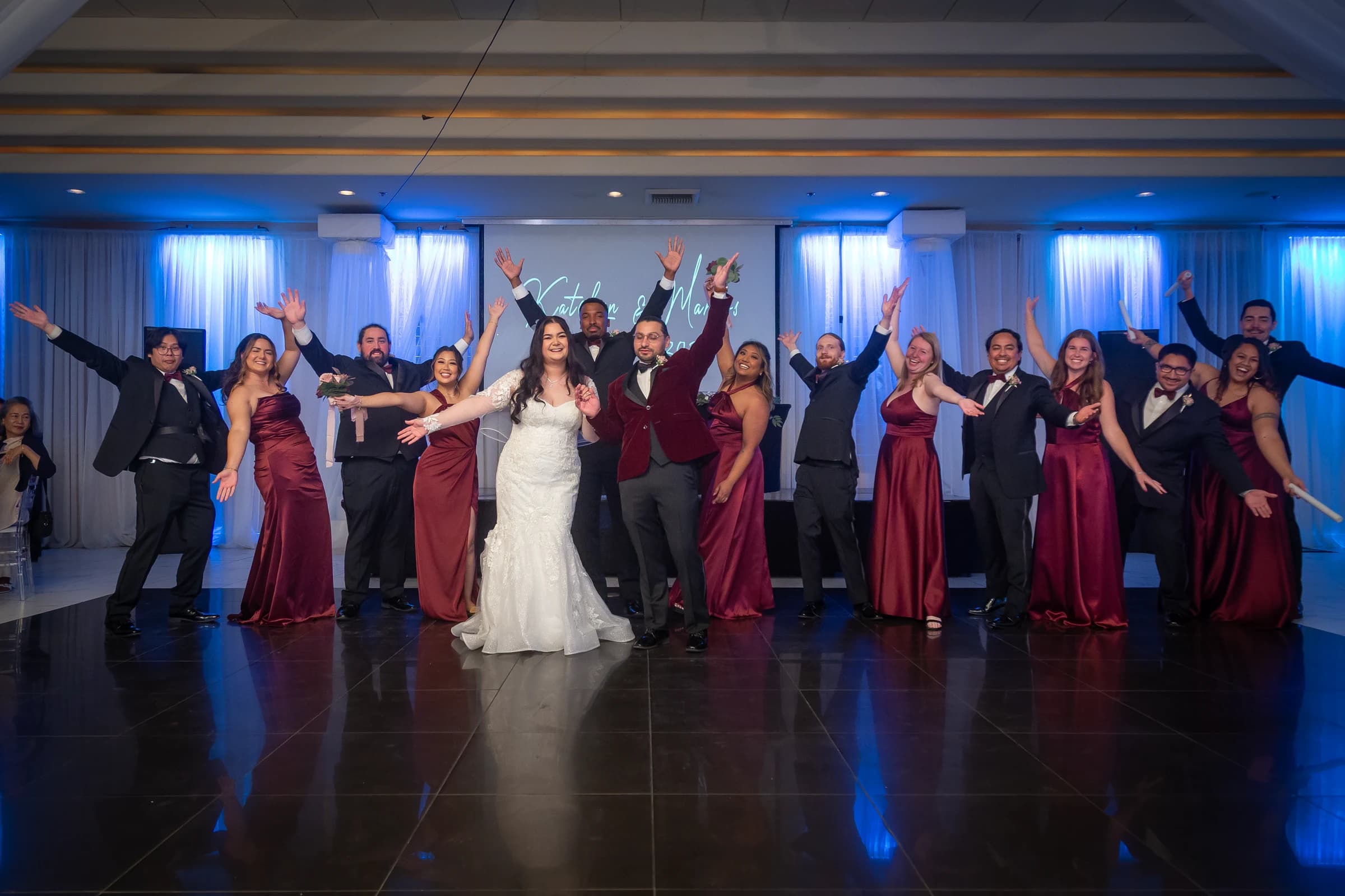 Newlyweds and their wedding party celebrate together on a blue-lit dance floor